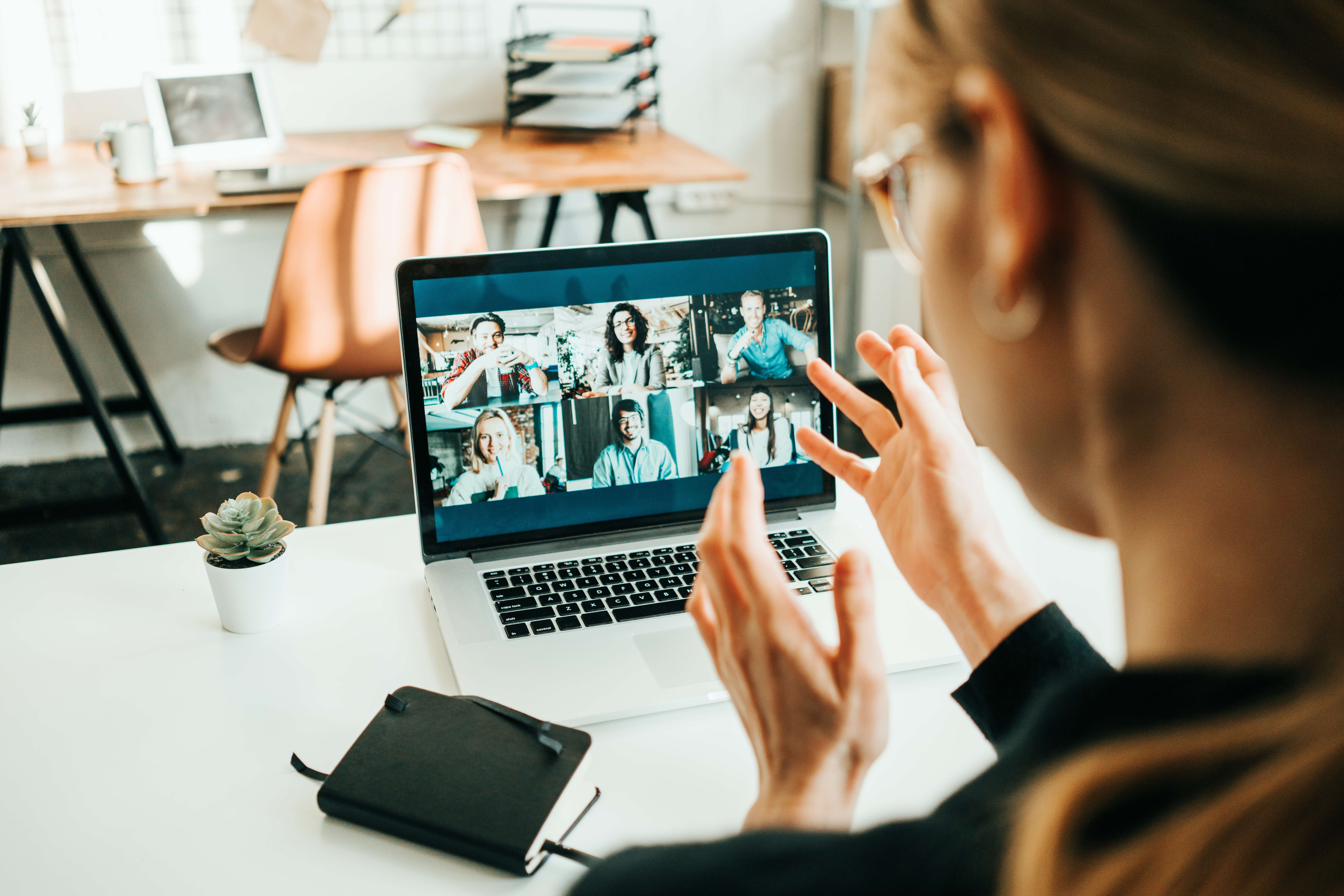 Woman has video call with her remote teammates using laptop. White loft workspace